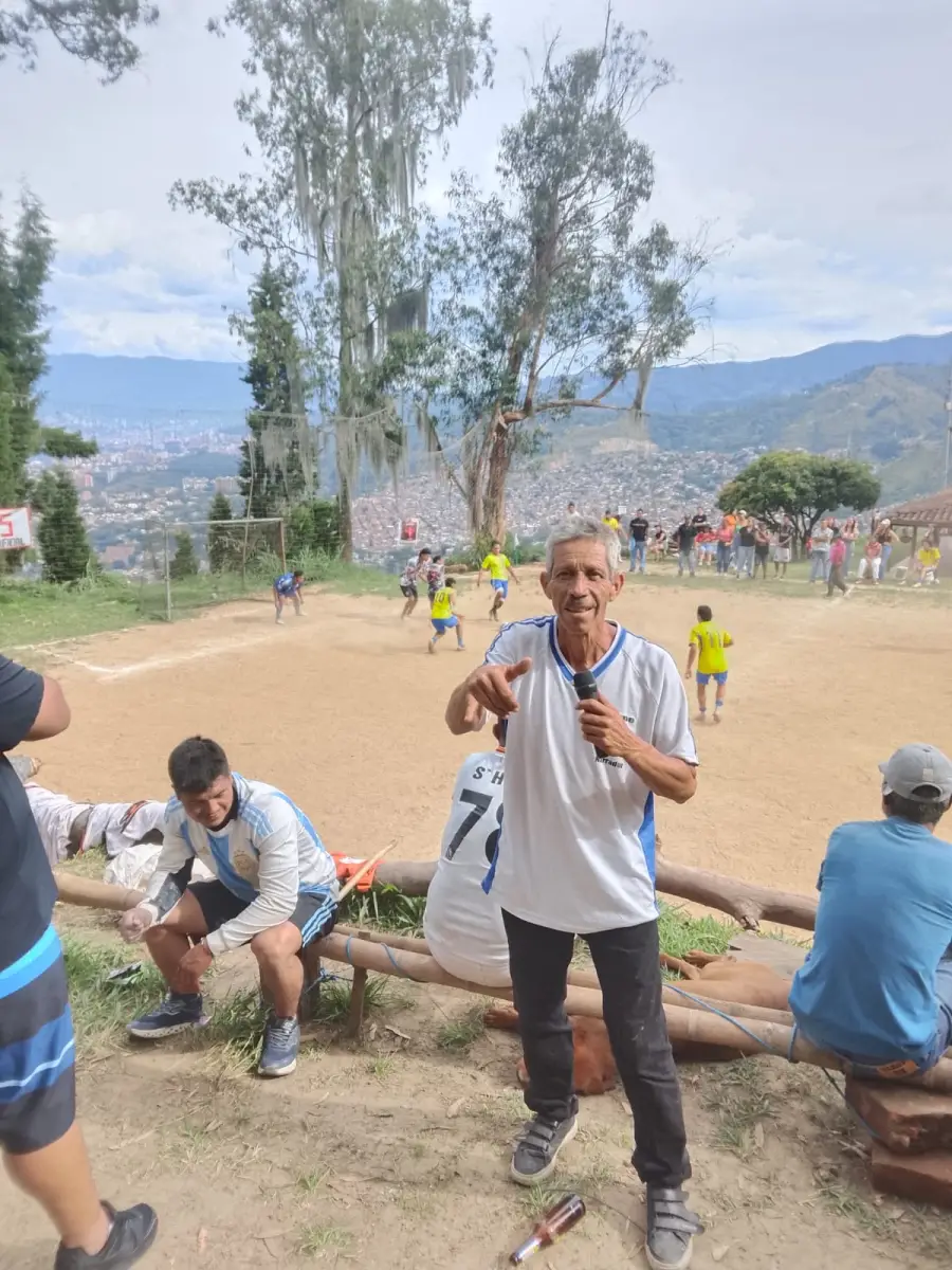Jaime Ramirez con micrófono en una cancha de tierra durante un torneo, con jugadores y público detrás